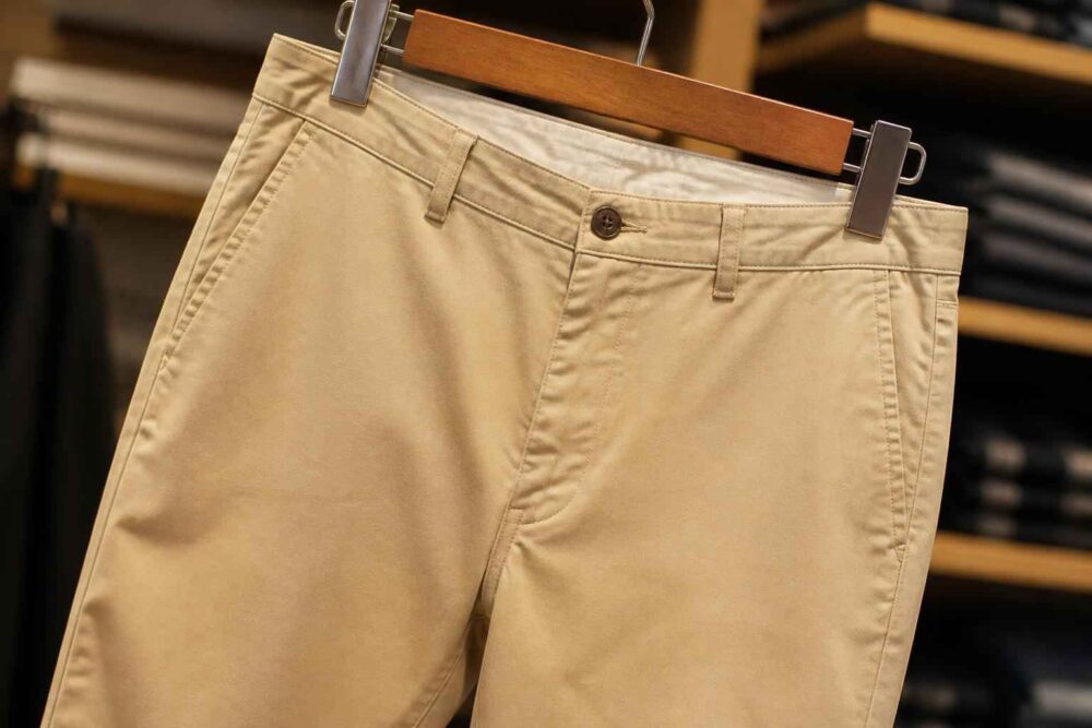 Beżowe spodnie chino na drewnianym klipsowym wieszaku Beżowe spodnie chino zawieszone na drewnianym wieszaku w sklepie odzieżowym